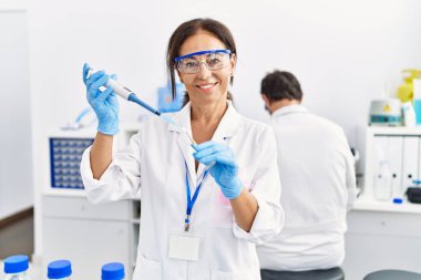 Orta yaşlı erkek ve kadın partnerler laboratuarda pipet ve test tüpü kullanarak bilim adamı üniforması giyerler.