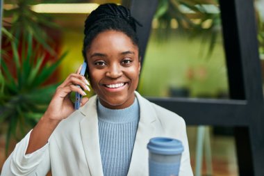 Genç Afrikalı Amerikalı iş kadını akıllı telefondan konuşuyor ve şehirde kahve içiyor..