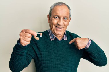 Yakışıklı, gri saçlı, tıbbi işitme cihazı olan, mutlu ve gururlu bir kişiyi işaret eden yaşlı bir adam. 