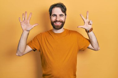 Sakallı, sıradan sarı tişörtlü, beyaz bir adam 8 numaralı parmaklarıyla gülümseyerek, kendinden emin ve mutlu görünüyor.. 