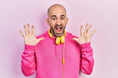 Spor kıyafetleri giyen, kulaklık takan genç kel adam çılgın kutlamalar yapıyor ve başarıya hayret ediyor. Kolları açık, gözleri açık, heyecanla bağırıyor. Kazanan konsept 