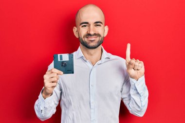 Elinde disket tutan genç kel bir adam bir fikir ya da soruyla gülümsüyor ve mutlu bir yüzle işaret ediyor. 