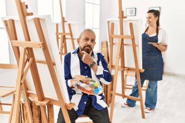 Sanat stüdyosundaki kıdemli sanatçı kameraya kollarını kavuşturup gülümseyen ve çenesini kaldıran kendinden emin bir şekilde bakıyor. Olumlu düşünmek. 