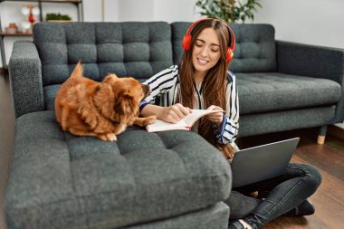 Genç İspanyol kadın dizüstü bilgisayar kullanıyor. Evde köpekle oturuyor.
