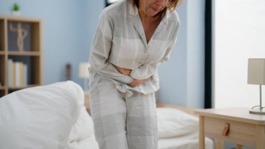 Orta yaşlı İspanyol kadın yatak odasında karın ağrısı çekiyor.