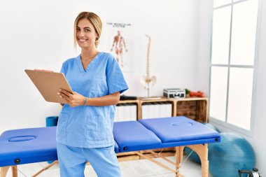 Kafkas fizyoterapist kadın klinikteki kontrol listesine mutlu bir şekilde yazıyor.