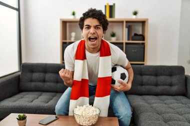 Genç İspanyol adam futbol maçı izliyor ve takımını evde destekliyor..