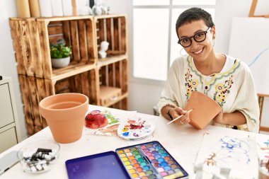 Sanat atölyesinde kilden seramik boyarken gülümseyen genç İspanyol kadın.