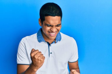 Gündelik giysiler giyen genç, yakışıklı İspanyol adam kolları havada ve gözleri kapalı bir şekilde başarıyı kutluyor ve şaşırıyor. 