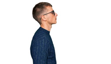 Gündelik kıyafetler ve gözlük takan genç sarışın adam yan tarafa bakıyor, rahat poz veriyor kendine güvenen bir gülümsemeyle doğal bir yüz ifadesi sergiliyor.. 