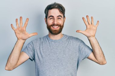 Sakallı, gri tişörtlü beyaz bir adam on numarayı gösteriyor ve gülümsüyor. Kendinden emin ve mutlu.. 