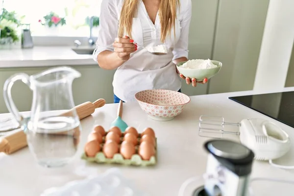 年轻的金发女人在厨房里往碗里倒面粉 — 图库照片