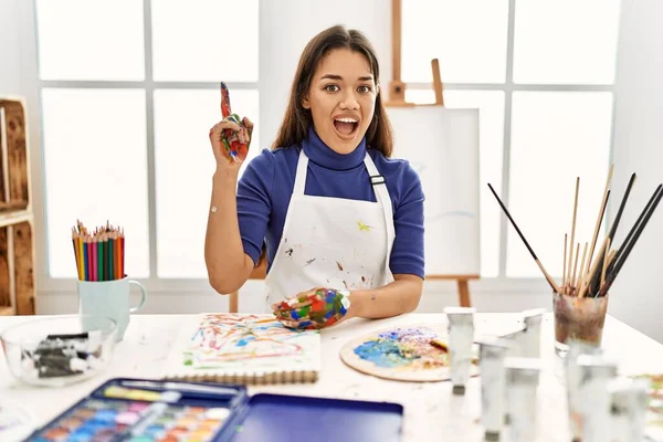 艺术工作室里的年轻的黑发女人 手绘着彩绘 指指点点 想出了个好主意 又兴奋又快乐第一大 — 图库照片