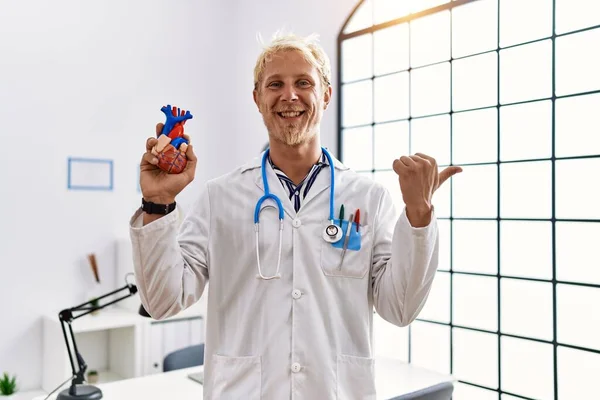 Giovane Uomo Biondo Indossa Medico Uniforme Tenendo Cuore Clinica Puntando — Foto Stock