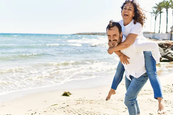 Hombre Hispano Mediana Edad Sonriendo Feliz Sosteniendo Mujer Espalda Playa —  Fotos de Stock