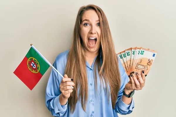 年轻的金发女子举着葡萄牙国旗和欧元钞票欢庆胜利 睁大眼睛惊呼 兴奋极了 — 图库照片