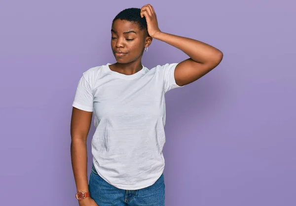 カジュアルな白いTシャツを着た若いアフリカ系アメリカ人女性は 質問を混乱させ 疑問に思っています 疑いもなく頭に手を置いて考える 包括的な概念は — ストック写真