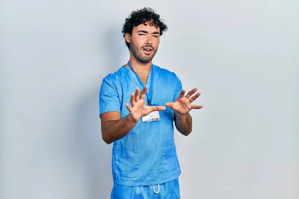 青い男看護師の制服を着て若いヒスパニック系の男は嫌悪反応のため 嫌悪感と恐ろしい嫌悪感の表情をうんざりし 嫌な顔をする 手を挙げて — ストック写真