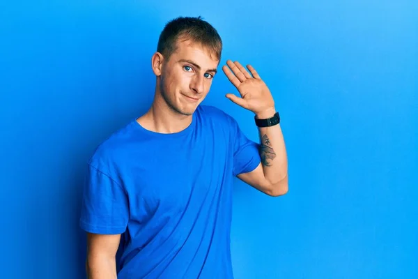 カジュアルブルーのTシャツを着た若い白人男性が挨拶をしながら笑顔で 優しい歓迎のジェスチャー — ストック写真