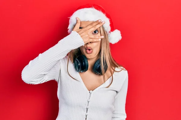 Красивая Латиноамериканка Рождественской Шляпе Наушниках Подглядывающая Шокирующие Закрывающие Лицо Глаза — стоковое фото
