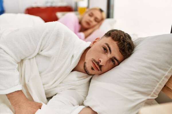 Young caucasian couple lying on the bed. Man looking to the camera at home.