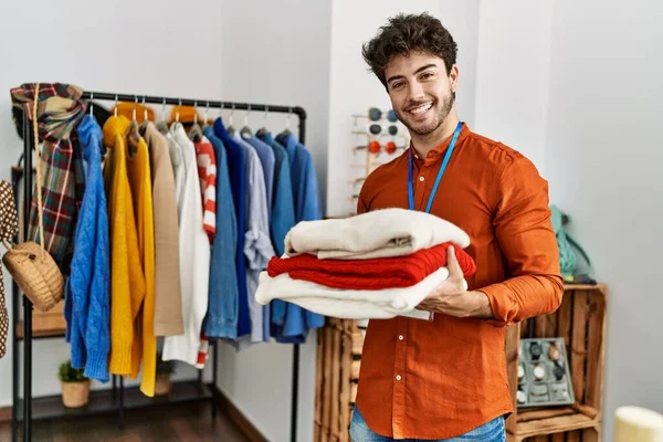 Joven Comerciante Hispano Sonriendo Feliz Sosteniendo Pila Suéter Tienda Ropa — Foto de Stock