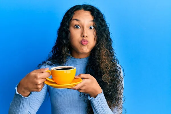 年轻的拉丁女人拿着咖啡 脸上带着滑稽的表情 嘴被空气吹胀 — 图库照片