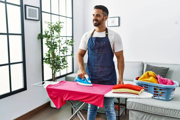 Ung Latinamerikansk Man Ler Säker Strykning Kläder Hemma — Stockfoto