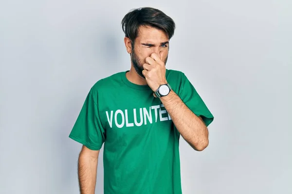 Jovem Hispânico Vestindo Camiseta Voluntária Cheirando Algo Fedorento Nojento Cheiro — Fotografia de Stock
