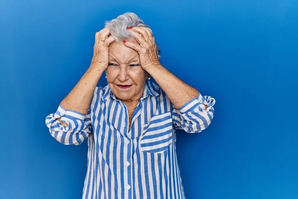 头发灰白的老妇人站在蓝色的背景上 由于疼痛和偏头痛 绝望和压力重重 手放在头上 — 图库照片