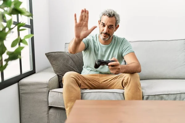 中年的他惊慌失措的男人坐在沙发上玩电子游戏 张开手做停止手势 表情严肃而自信 手势防守 — 图库照片