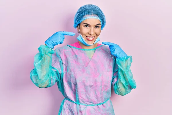 身穿外科制服和医疗面罩的年轻黑发女子面带微笑 露出愉快的表情 用手指 牙齿和嘴指尖 牙齿健康概念 — 图库照片