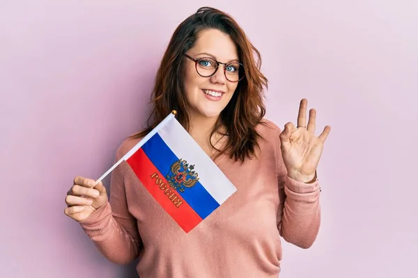 ロシア連邦旗を持っている若い白人女性は指でOkサインをします 笑顔優しいジェスチャー優れたシンボル — ストック写真