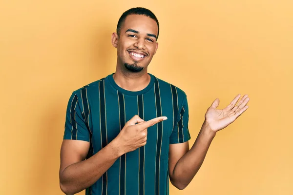 手で提示し 指で指している間若いアフリカ系アメリカ人の男性は カジュアルな服を着てカメラに驚いて笑顔 — ストック写真