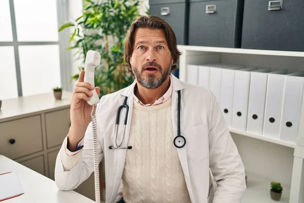 Bonito Médico Meia Idade Falando Telefone Clínica Assustado Surpreso Com — Fotografia de Stock