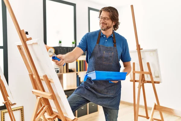 中年白人男子在艺术工作室用彩绘滚筒微笑而自信地画画 — 图库照片