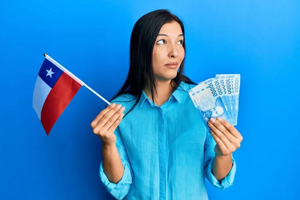 年轻的拉丁女人拿着儿童旗和儿童比索钞票 面带微笑地看着旁边 目不转睛地想着 — 图库照片
