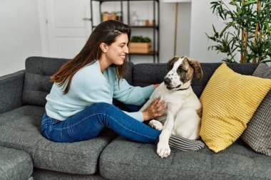 Genç bir kadın evdeki kanepede oturan köpeğe sarılıyor.