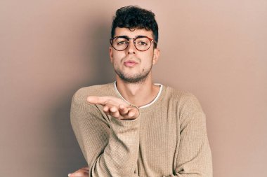 Gündelik kıyafetler giyen ve gözlüklü genç İspanyol adam kameraya bakıp havada el sallayarak öpüşüyor ve çok güzel ve seksi. aşk ifadesi. 