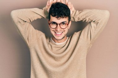 Genç İspanyol bir adam günlük kıyafetler ve gözlük takıyor komik ve çılgın poz veriyor parmakları tavşan kulağı gibi, neşeli gülümsüyor 