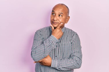 Orta yaşlı, sıradan kıyafetler giyen, elleri çenesinde soru soran, düşünceli bir Latin adam. Düşünceli bir yüzle gülümsüyor. şüphe kavramı. 