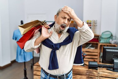 Butik dükkanında alışveriş torbaları tutan yakışıklı bir adam. Eli yüzü asık, şaşırmış ve sinirli bir halde. 