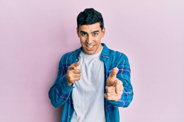 Sıradan kıyafetler giyen yakışıklı İspanyol adam mutlu ve komik yüzlü parmaklarını kameraya doğrultuyor. iyi enerji ve titreşimler. 