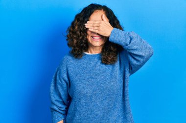 Orta yaşlı İspanyol kadın, sıradan kıyafetler giyiyor, gülümsüyor ve yüz yüze gülüyor. Şaşırtmak için gözleri örtüyor. kör kavram. 