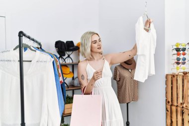 Genç beyaz kadın elbise mağazasından kendine güvenen bir şekilde gülümsüyor.