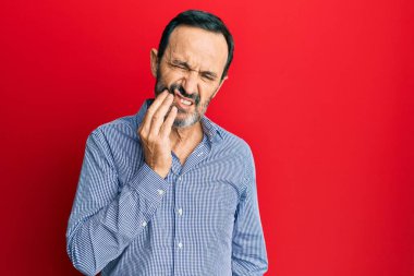 Orta yaşlı İspanyol bir adam diş ağrısı ya da diş hastalığından dolayı dişleriyle dudaklarına dokunarak acı dolu bir ifade sergiliyor. dişçi 