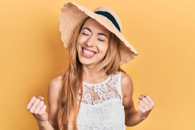 Yazlık şapkalı, mutlu ve heyecanlı genç beyaz bir kadın kolları havada, gülümseyen ve başarı için bağıran bir jest yapıyor. kutlama konsepti. 