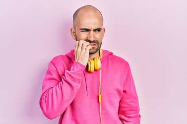 Spor kıyafetleri giyen, kulaklık takan, stresli ve gergin görünen elleri ağız yiyen genç kel bir adam. anksiyete. 