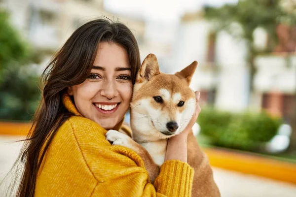 Güzel genç bir kadın parkta mutlu Shiba Inu köpeğine sarılıyor.