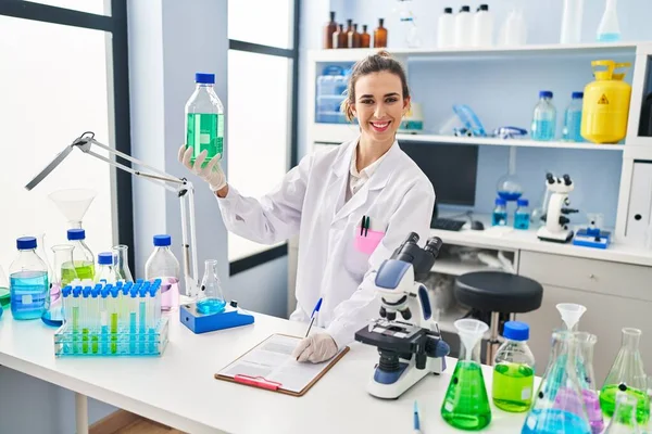 Young Woman Wearing Scientist Uniform Holding Bottle Writing Report Laboratory — Stock Photo, Image